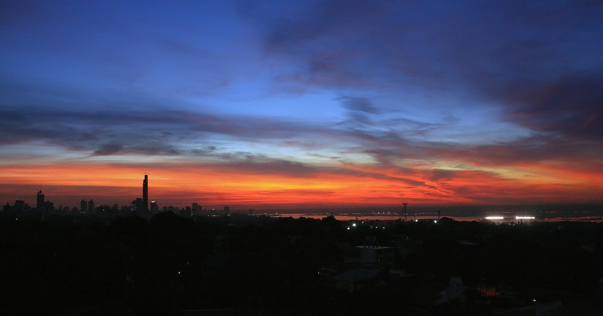 Silueta de los edificios de Asunción bajo un cielo con nubes, al caer la tarde, con el río al fondo