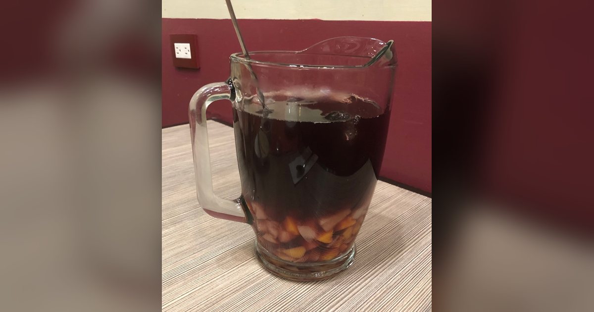 Jarra de clericó con frutas picadas y una cuchara larga sobre una mesa