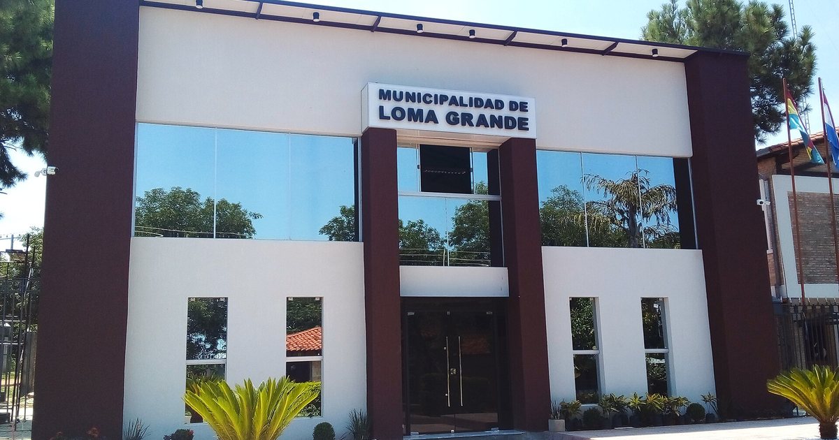 La fachada de la Municipalidad de Loma Grande, con ventanales de vidrio, columnas marrones y dos banderas en mástiles