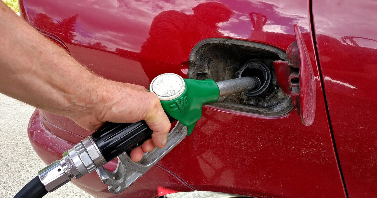 Una mano carga combustible con el pico del surtidor en el tanque de un auto
