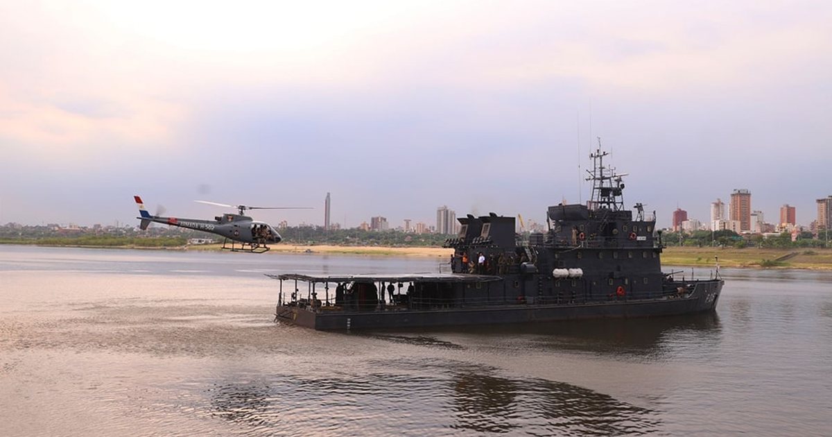 El patrullero P05 Itaipú de la Armada Paraguaya navega por el río, con un helicóptero en vuelo a su lado