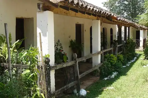 Foto: Diana Sanabria / Wikimedia Commons · dominio público Casa antigua de Caapucú con techo de tejas, galería sobre pilares blancos y un jardín junto a una calle empedrada