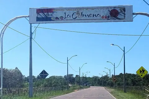 Arco de bienvenida de La Colmena sobre el ramal de acceso, con saludos en castellano, guaraní, inglés y japonés