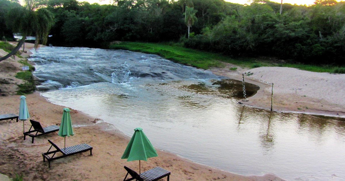 Arroyo Yhaguy que corre sobre lajas junto a una playa de arena con reposeras y sombrillas verdes, en un balneario de Valenzuela