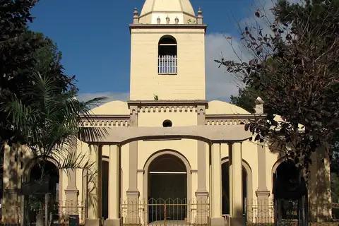 Fachada amarilla de la iglesia Virgen del Rosario de Yataity, con su torre y una cúpula blanca, detrás de una reja