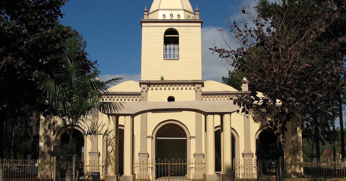 Fachada amarilla de la iglesia Virgen del Rosario de Yataity, con su torre y una cúpula blanca, detrás de una reja