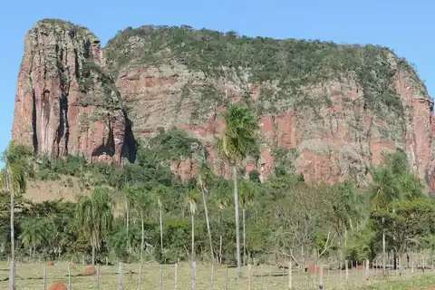 Paredones de roca rojiza del Cerro Memby, con palmeras y un camino de tierra al pie