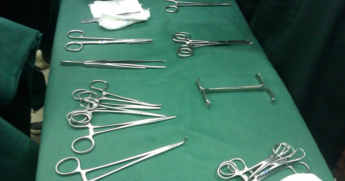Pinzas, tijeras y otros instrumentos quirúrgicos ordenados sobre un paño verde, listos para una operación