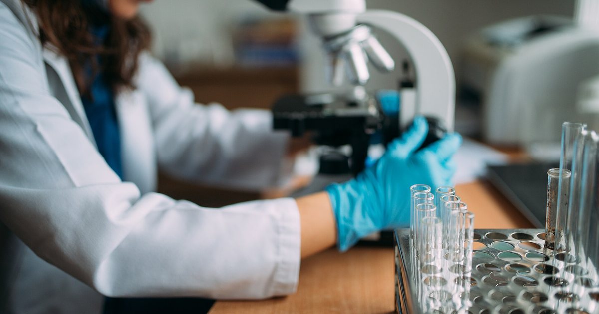 Una profesional con guantes trabaja con un microscopio y tubos de ensayo en un laboratorio de análisis clínicos