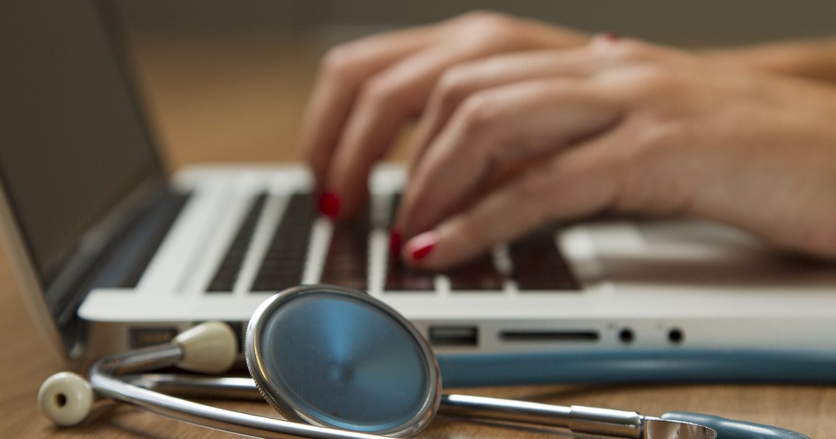 Un estetoscopio sobre un escritorio, frente a una computadora portátil en uso
