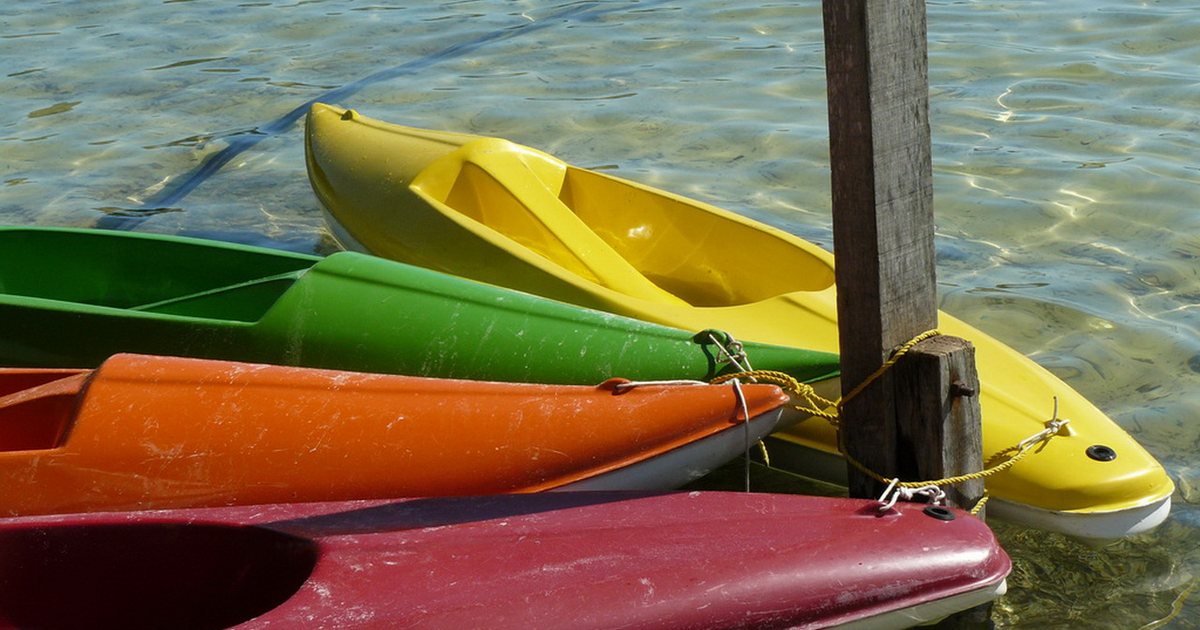 Kayaks de colores amarrados a un poste de madera en el agua transparente de la Laguna Blanca
