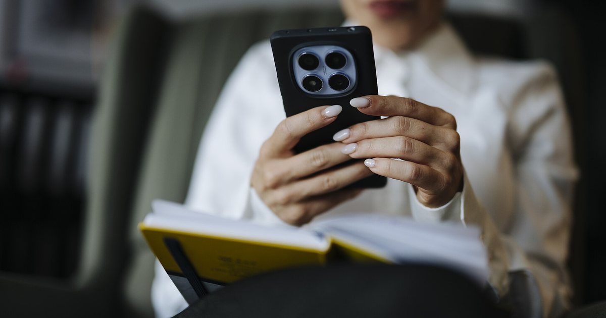 Manos de una persona que usa el celular, con una libreta abierta sobre las piernas