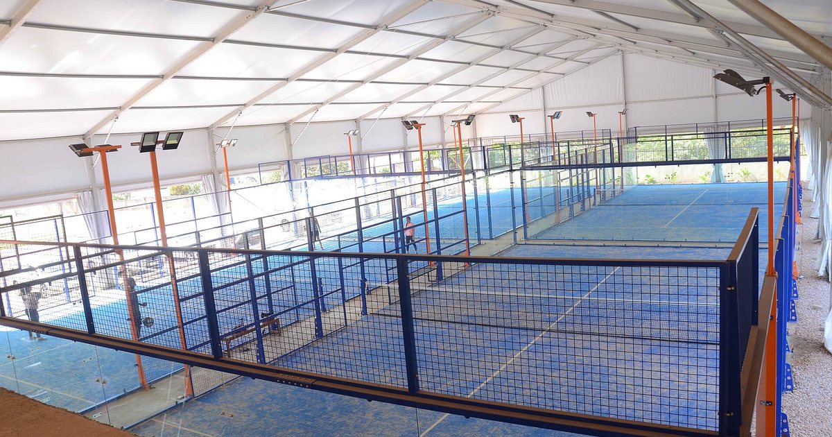 Canchas de pádel techadas, con piso azul y paredes de vidrio y reja