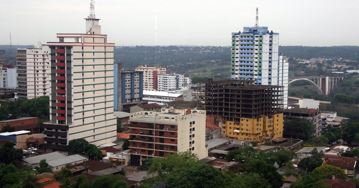Edificios del centro de Ciudad del Este bajo un cielo nublado, con el Puente de la Amistad al fondo