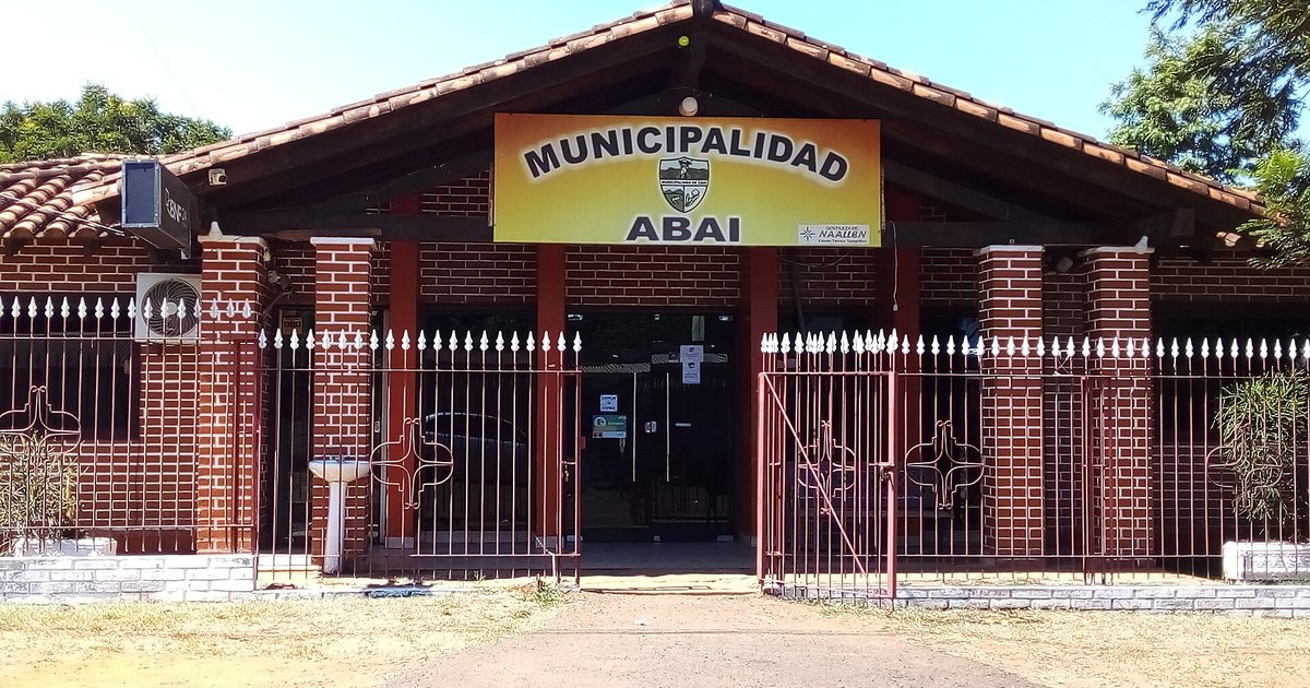 Edificio de ladrillo de una planta con techo de tejas, rejas blancas y el letrero amarillo de la Municipalidad de Abaí
