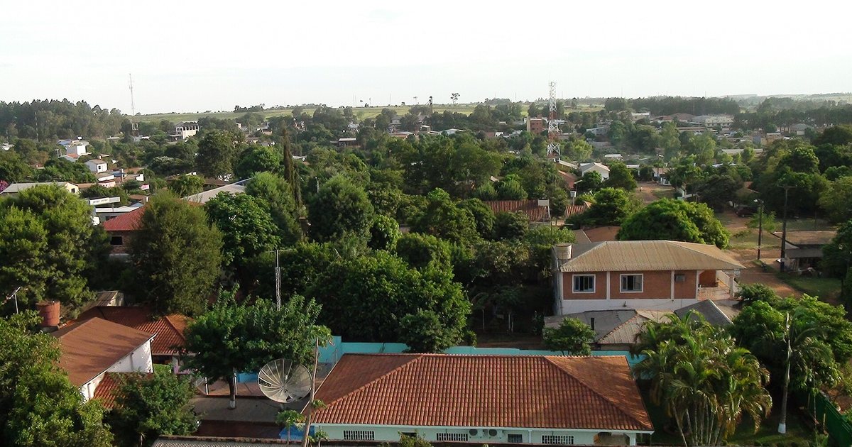 Vista de Campo 9 desde lo alto, con casas de techo de tejas entre árboles, una antena parabólica y torres de comunicación hacia el horizonte, en Caaguazú