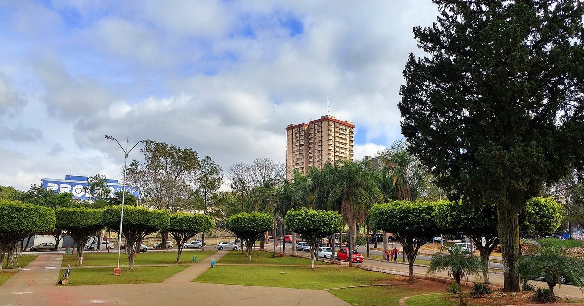 La plaza frente a la catedral de Ciudad del Este, con árboles podados en forma redonda, césped, una avenida y un edificio alto al fondo