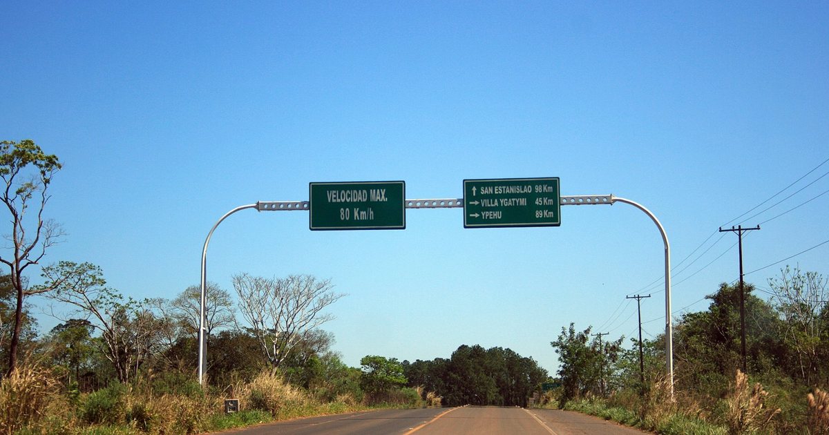 Ruta asfaltada cerca de Curuguaty con un pórtico de carteles verdes que marcan 80 km/h de velocidad máxima y las distancias a San Estanislao, Villa Ygatimí e Ypehú