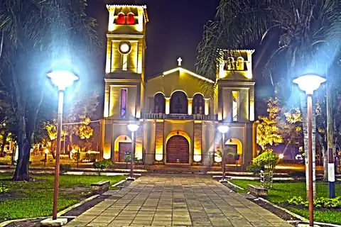 Foto: Raulzunini / Wikimedia Commons · CC BY-SA 4.0 Iglesia de Guarambaré iluminada de noche al fondo de la plaza Emiliano R. Fernández, con faroles y palmeras