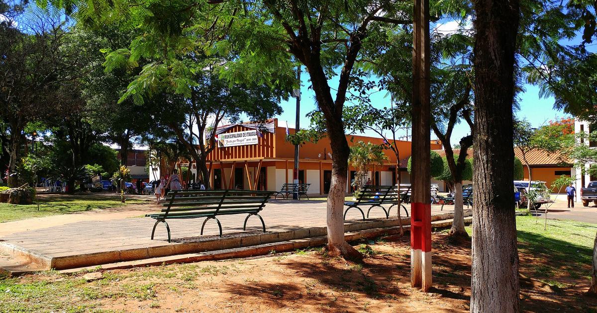 La plaza frente a la Municipalidad de Itauguá, con bancos verdes a la sombra de los árboles y el edificio municipal al fondo