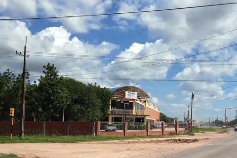 Sede de la Municipalidad de Loma Plata, con techo curvo y banderas, detrás de un muro de ladrillos junto a una avenida