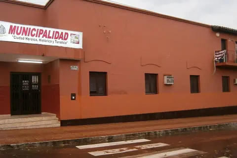 Foto: Ulises Icardi / Wikimedia Commons · CC BY-SA 4.0 Edificio de la Municipalidad de Piribebuy, de paredes color terracota, en una esquina con la calle mojada por la lluvia