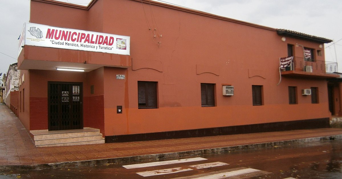 Edificio de la Municipalidad de Piribebuy, de paredes color terracota, en una esquina con la calle mojada por la lluvia