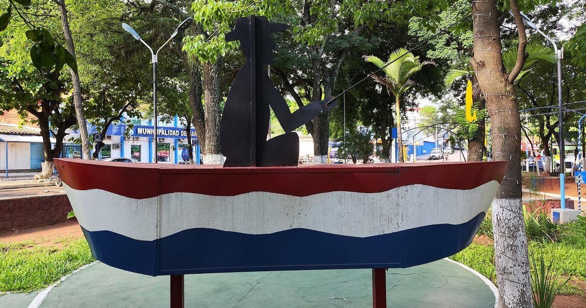 Monumento a los pescadores en la Plaza Central de San Antonio: una canoa pintada con los colores de la bandera paraguaya y la silueta negra de un pescador con su caña, entre árboles