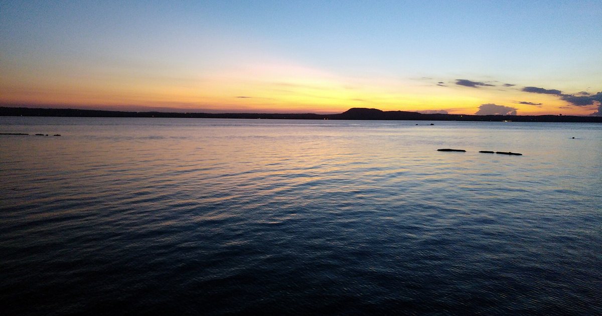 Atardecer sobre un lago en calma, con un cerro oscuro en el horizonte y el cielo naranja y azul