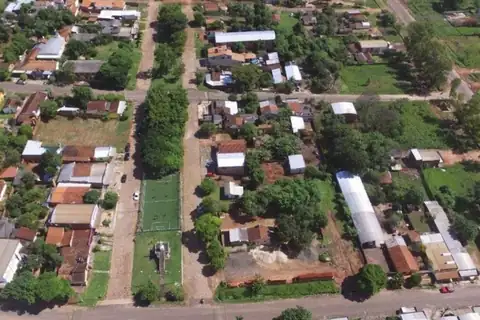 Vista aérea de un barrio con calles de tierra, casas con techos de chapa y teja, una cancha de pasto sintético y mucho arbolado