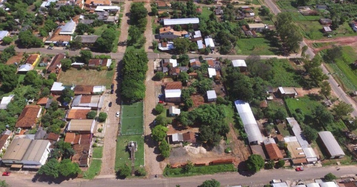 Vista aérea de un barrio con calles de tierra, casas con techos de chapa y teja, una cancha de pasto sintético y mucho arbolado