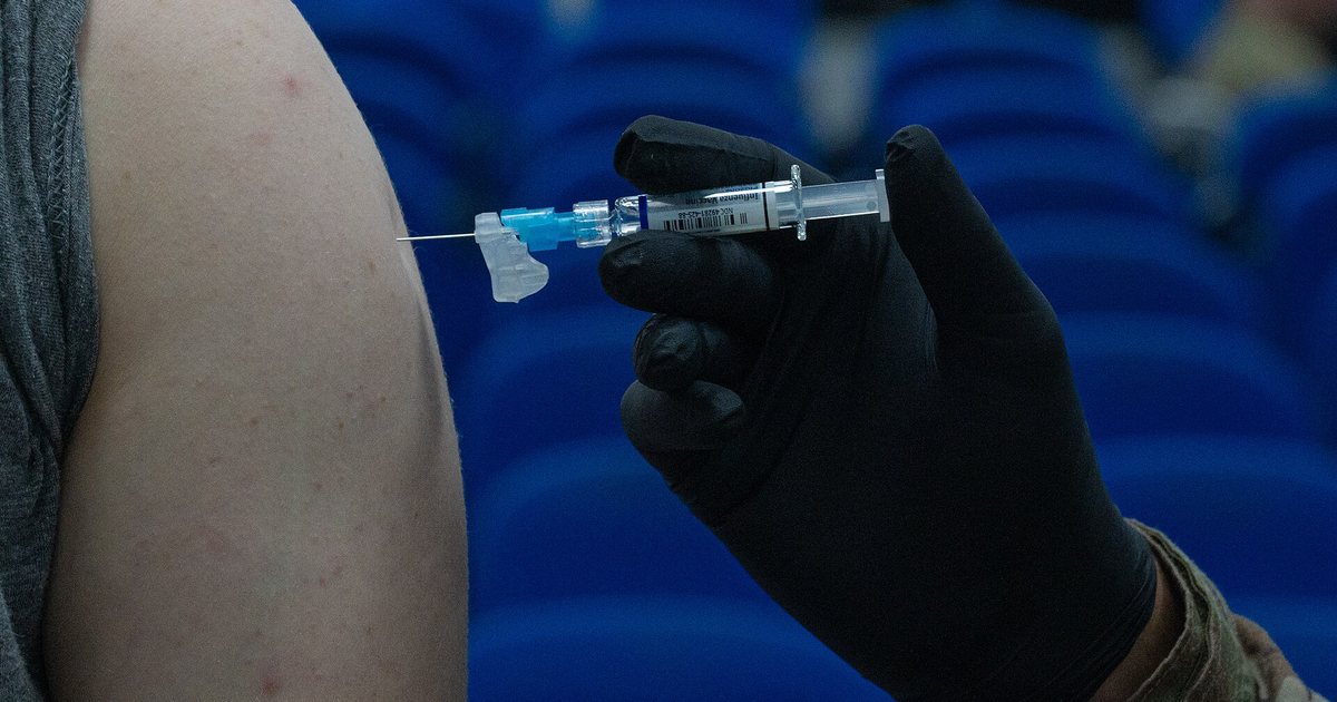 Una mano con guante aplica una vacuna contra la influenza en el brazo de un adulto